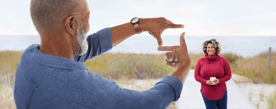 man holding hands out in front of him, using fingers to make a frame. Woman standing in background.